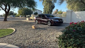 A maroon car parked in a driveway with a gravel surface, surrounded by a white wall and greenery. - Southwest-Chic 1BR Casita, Private Yard + Driveway, Northern Phoenix Getaway (Glendale)