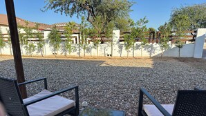 An outdoor seating area with two black metal chairs and a glass table, surrounded by gravel and trees. - Southwest-Chic 1BR Casita, Private Yard + Driveway, Northern Phoenix Getaway (Glendale)