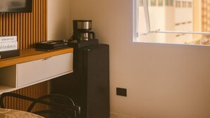 Une chambre d’hôtel compacte avec un mur en lambris de bois, un téléviseur à écran plat, une petite kitchenette, un coin repas avec une table à motifs et une fenêtre donnant sur la ville.