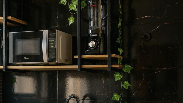 Une cuisine moderne dotée d’un plan de travail noir, d’un four à micro-ondes encastré, d’une machine à café et d’une étagère en bois ornée de plantes vertes.