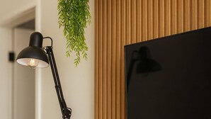 Un intérieur moderne avec un mur lambrissé en bois, une lampe de bureau noire, deux vases noirs, un téléviseur et un livre sur le thème du voyage.