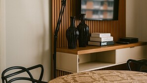 Un salon moderne avec une table ronde, des chaises noires, un lampadaire, un téléviseur posé sur une étagère en bois et des vases décoratifs.