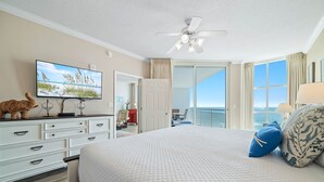 A hotel room with a bed, a television, a ceiling fan, a dresser, and a view of the ocean through a sliding door. - Palacio 403 | Beachfront | My Beach Getaways (Pensacola)
