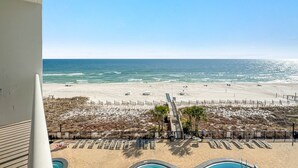A beach view from a balcony with a pool area, sandy beach, and a fence separating the beach from the pool. - Palacio 403 | Beachfront | My Beach Getaways (Pensacola)