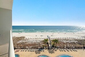Une vue sur la plage depuis un balcon donnant sur une piscine, une plage de sable et une clôture qui sépare la plage de la piscine.