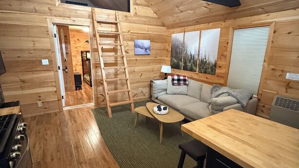 Ein gemütliches Blockhauss-Interieur mit Holzboden, einer Couch, einem Couchtisch, einer Leiter und einem Gemälde an der Wand.
