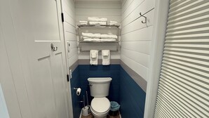 Ein schmales Badezimmer mit Toilette, Handtuchregalen und einer Tür mit Griff.