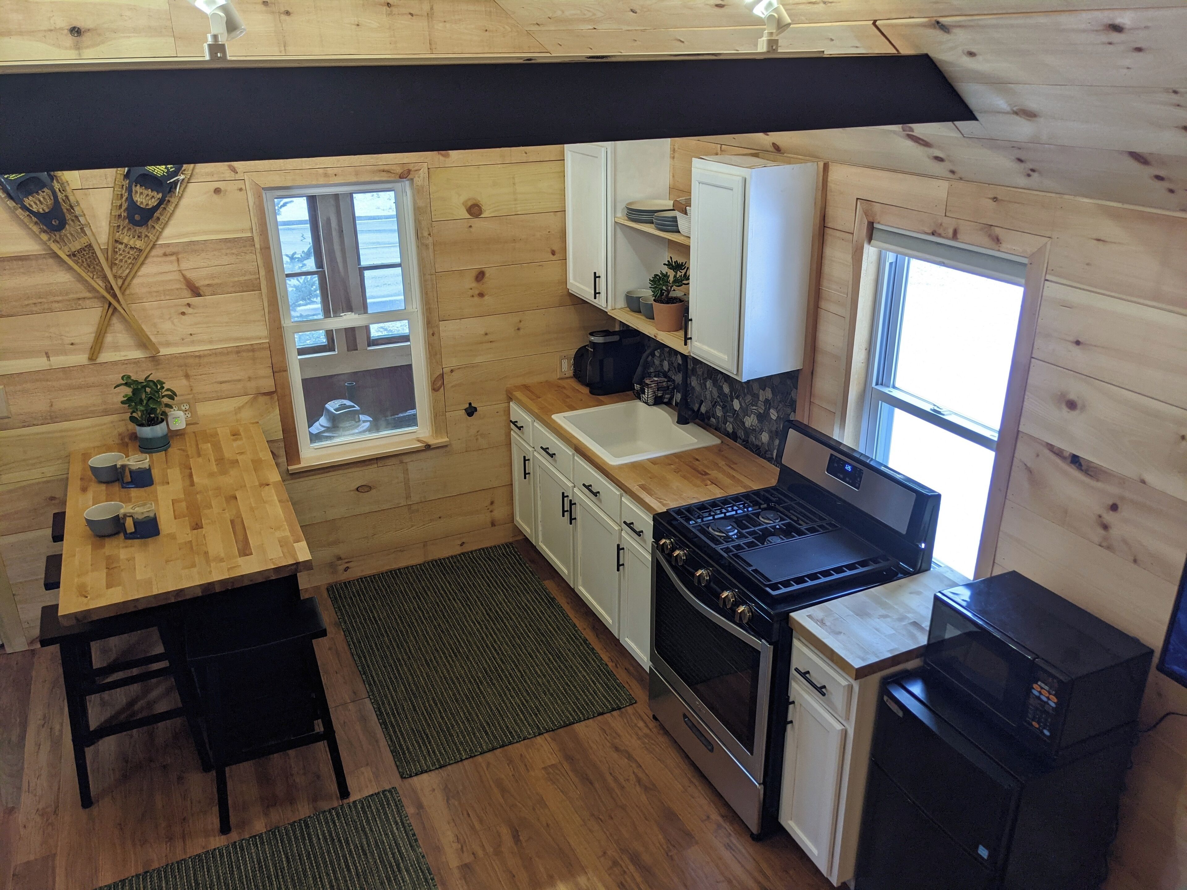 A compact kitchen with wooden walls, a stove, microwave, and a sink.