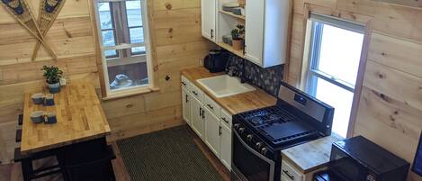 A compact kitchen with wooden walls, a stove, microwave, and a sink.
