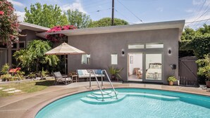 Une maison moderne dotée d’une piscine, d’un patio couvert et d’une chambre visible à travers des portes vitrées.