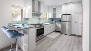 Une cuisine moderne avec des meubles blancs, des appareils en acier inoxydable et un coin bar doté de chaises bleues.