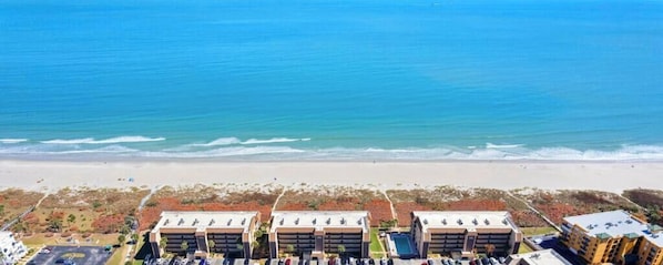 Et hotel ved stranden med flere bygninger, parkeringsplads og udsigt over havet.