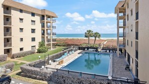 Zona de piscina con vistas a la playa, rodeada de edificios de apartamentos.