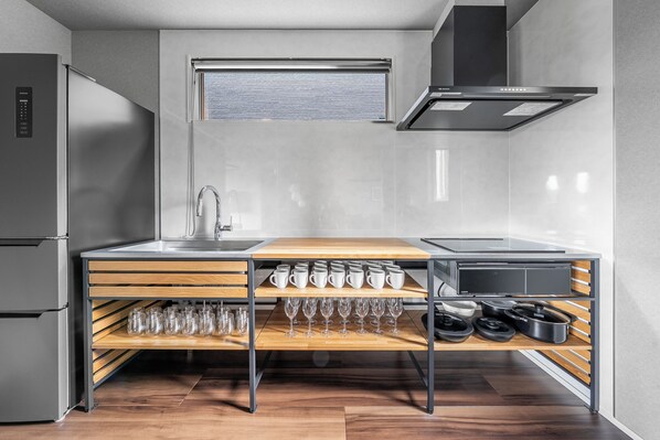 Una cocina compacta con un refrigerador de acero inoxidable, horno empotrado, un lavamanos y un estante de madera con cristalería.