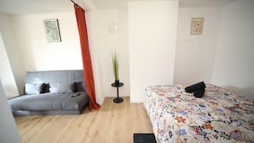 A modern bedroom with a grey sofa, a floral bedspread, a potted plant, and a red curtain.