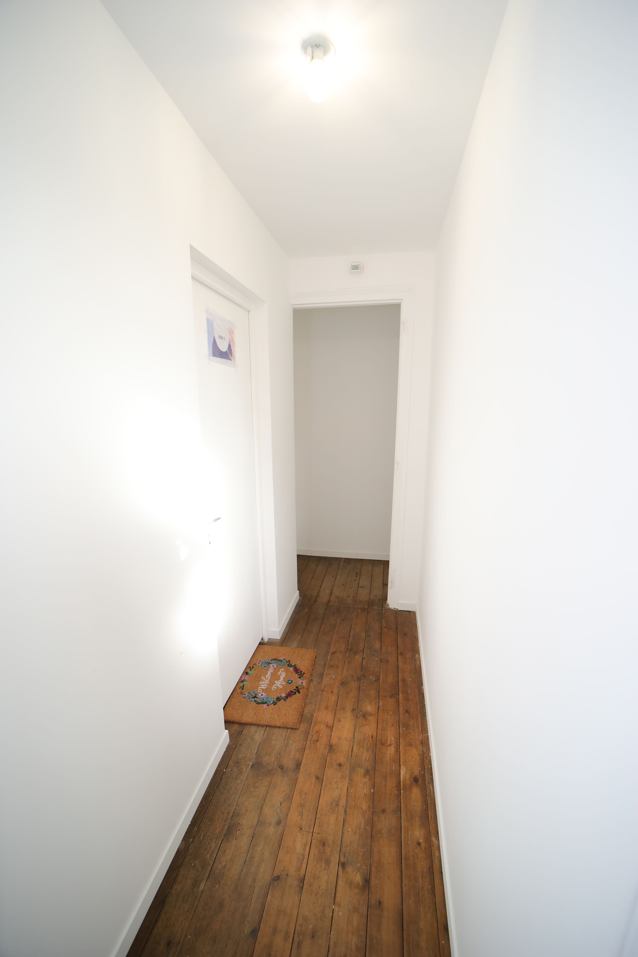 A narrow hallway with wooden flooring and white walls.