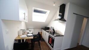 A compact kitchen with white cabinets, a black stove, and a small dining area with two chairs. - Eden (Cambrai)