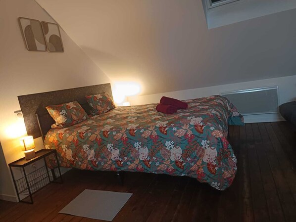A bedroom with a bed, a nightstand, a lamp, and a window. - Eden (Cambrai)
