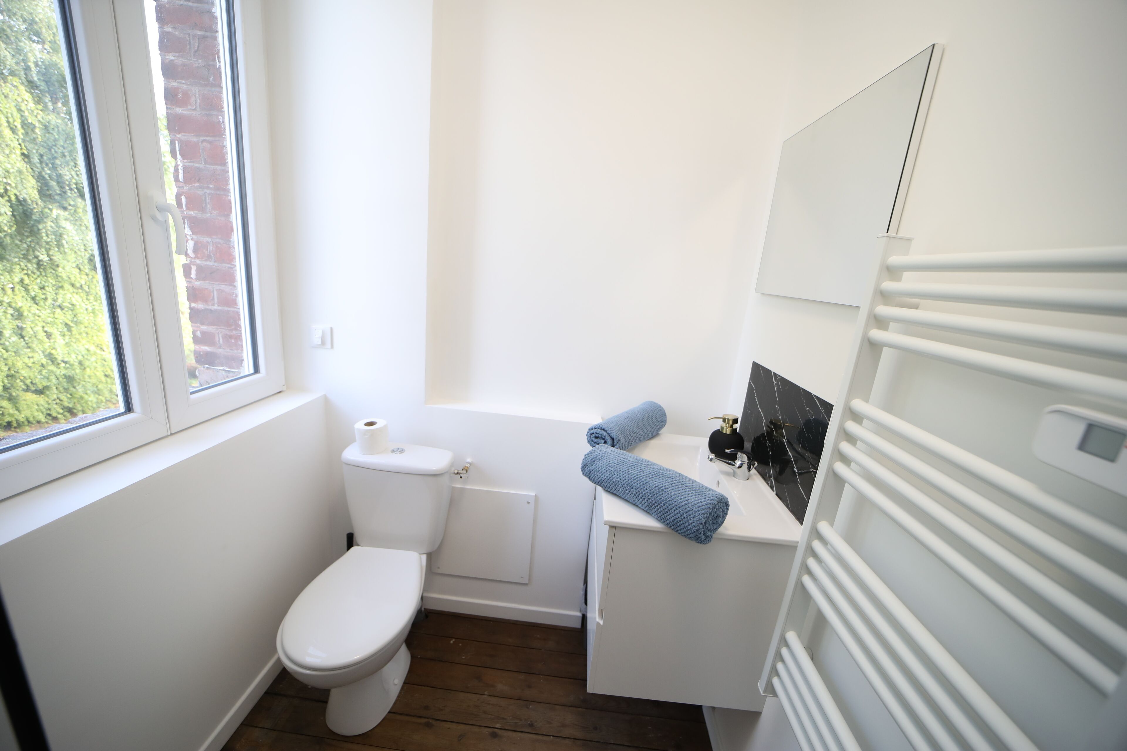 Ein kleines, helles Badezimmer mit Toilette, Waschbecken und Handtuchhalter in Weiß.