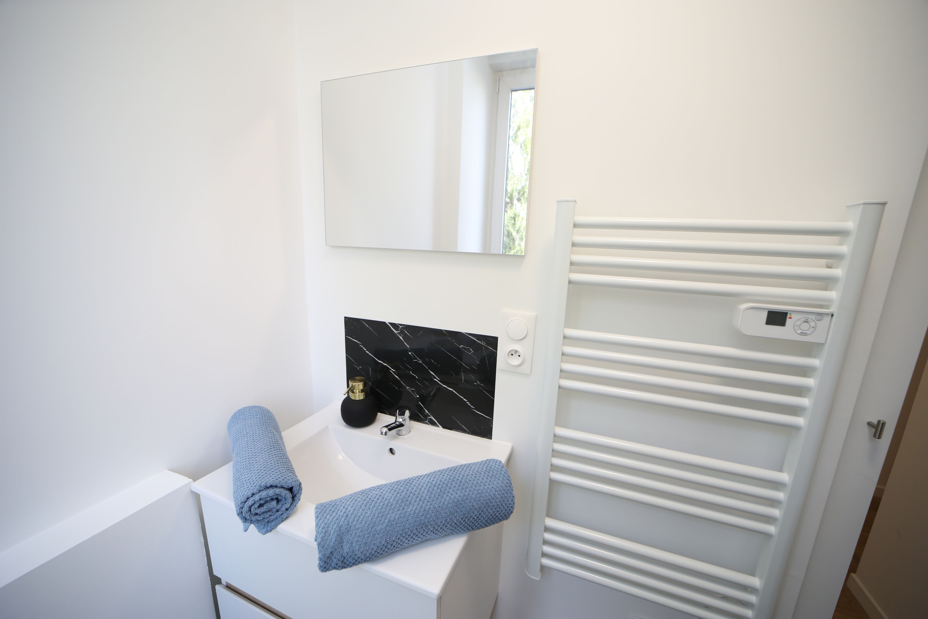 A modern bathroom with a white sink, a black marble backsplash, a white towel, and a white towel rack.