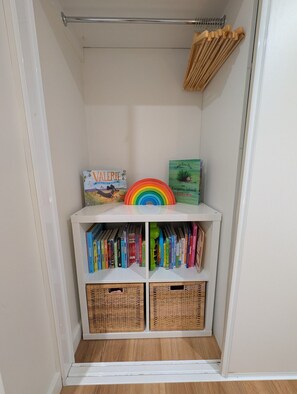 Een kleine, witte opbergruimte met een metalen stang, eenhoorn speelgoed en kinderboeken.