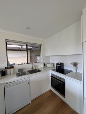 A modern kitchen with white cabinetry, a built-in dishwasher, a stove, and a window above the sink. - Sails: Family-friendly, in the heart of town (Kingscote)