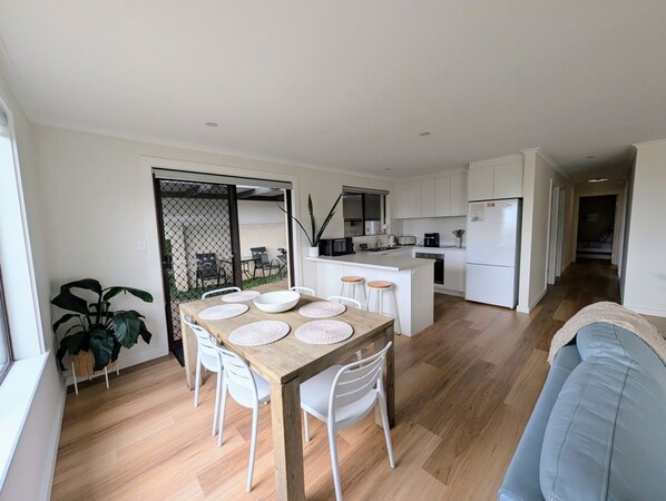 A modern kitchen with white cabinets, a dining area with a wooden table and white chairs, and a blue sofa in the living area.