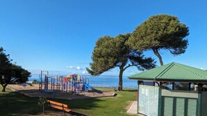 Un parque infantil con tobogán y estructuras para escalar, una banca y un pabellón cerca de una masa de agua.