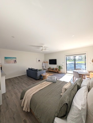 A modern bedroom with a bed, a sofa, a TV, and a dining area with a view.