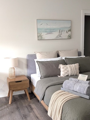 A bedroom with a bed, bedside table, lamp, and a painting on the wall.