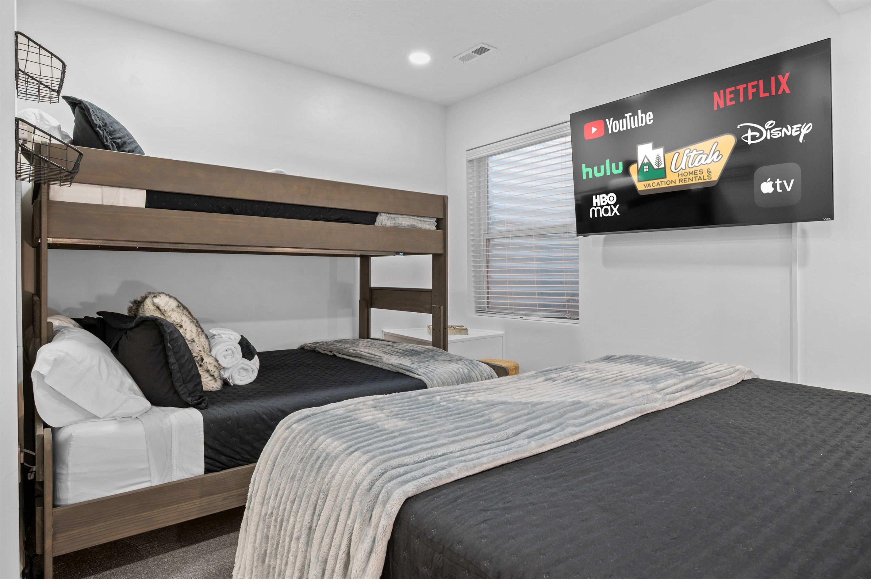 Une chambre avec un lit superposé, un téléviseur à écran plat diffusant divers services de streaming et une fenêtre avec des stores.