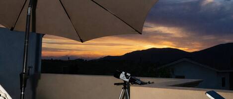 A patio with a telescope, a grill, and a large umbrella.