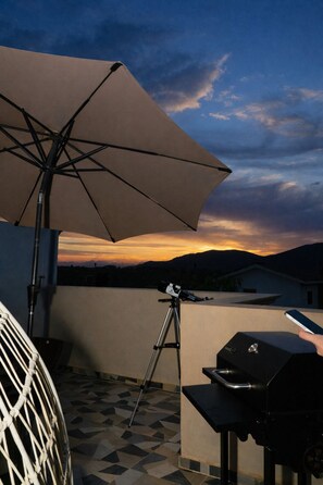 Eine Terrasse mit Teleskop, Grill und einem großen Sonnenschirm.