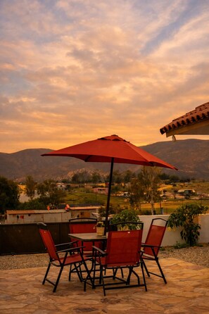 Eine Terrasse im Freien mit Tisch und Stühlen, einem roten Sonnenschirm und Blick auf eine Berglandschaft.