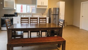 Een kleine keuken met witte kastjes, een roestvrijstalen koelkast en een eettafel met stoelen.