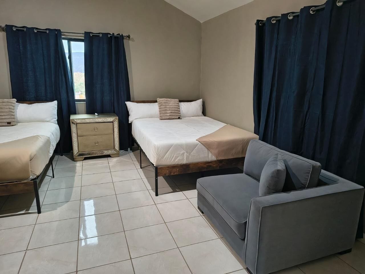A bedroom with two beds, a nightstand, a sofa, and a window with curtains.