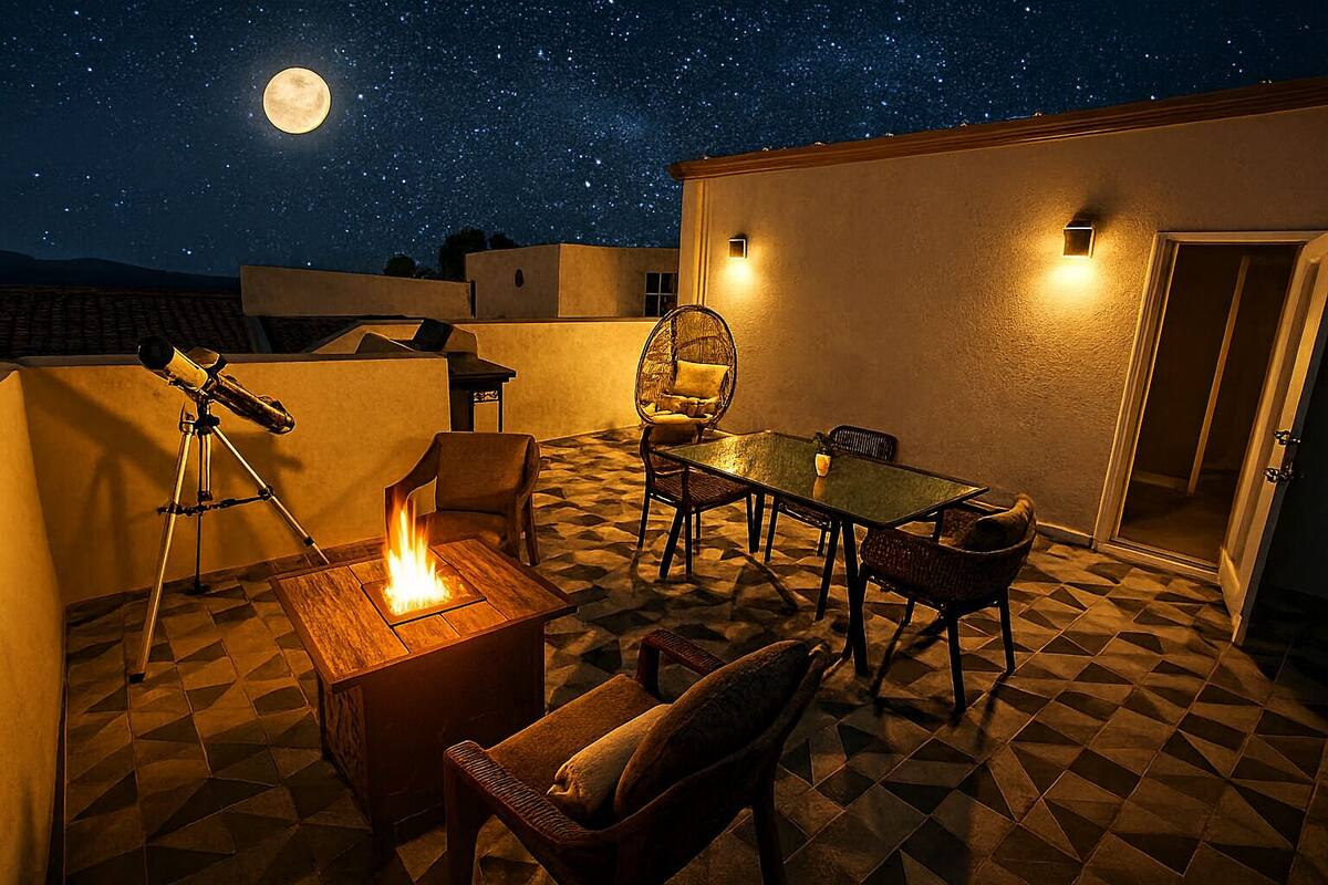 Un patio en la azotea con un telescopio, una chimenea y una zona de comedor bajo un cielo estrellado.