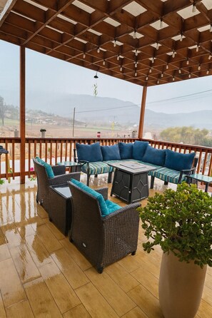 Eine Terrasse im Freien mit Korbmöbeln, einem großen Topfpflanzen und Blick auf entfernte Hügel.