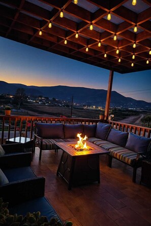 Eine Terrasse im Freien mit Feuerstelle, Holzmöbeln und Blick auf die Landschaft.