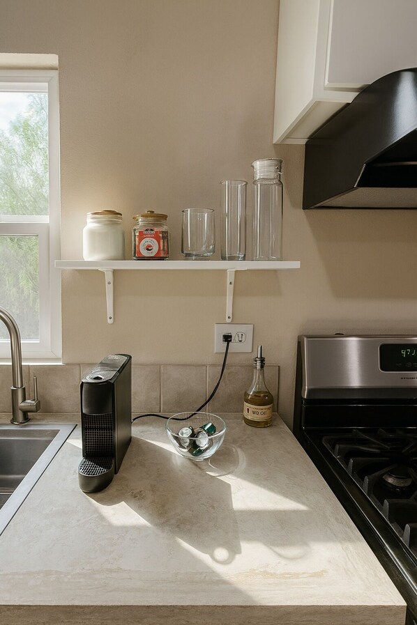 A kitchen with a built-in stove, a coffee maker, a glass bowl with ice, and a bottle of oil on the counter.