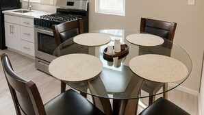 Een moderne keuken met een glazen eettafel, omringd door stoelen, een fornuis en kasten.