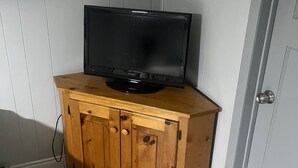 Un televisor sobre un mueble de madera en una habitación con paredes blancas y una puerta.