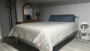 Un dormitorio con cama, mesita de noche con lámpara, espejo y perchero.