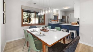 Una cocina moderna con armarios blancos, una isla grande y un comedor con una mesa blanca y sillas verdes.