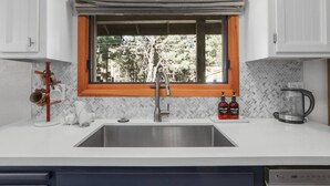 Una cocina con ventana, un lavamanos, una cafetera y dos botellas de detergente.
