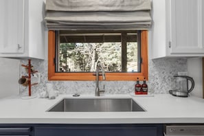 Una cocina con ventana, un lavamanos, una cafetera y dos botellas de detergente.