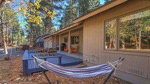 Una cabaña moderna con una hamaca, asientos exteriores y grandes ventanales con vistas a un bosque.
