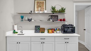 Een keuken met witte kastjes, een magnetron, een waterkoker en verschillende etenswaren op het aanrecht.