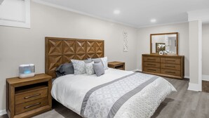 Slaapkamer met een houten hoofdbord, een bed met beddengoed met een patroon, een nachtkastje, een kaptafel en een spiegel.