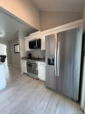 A modern kitchen with white cabinets, a stainless steel refrigerator, a microwave, and a gas stove. - Enchanting 4-bedroom house with spacious backyard and pool in El Paso (El Paso)